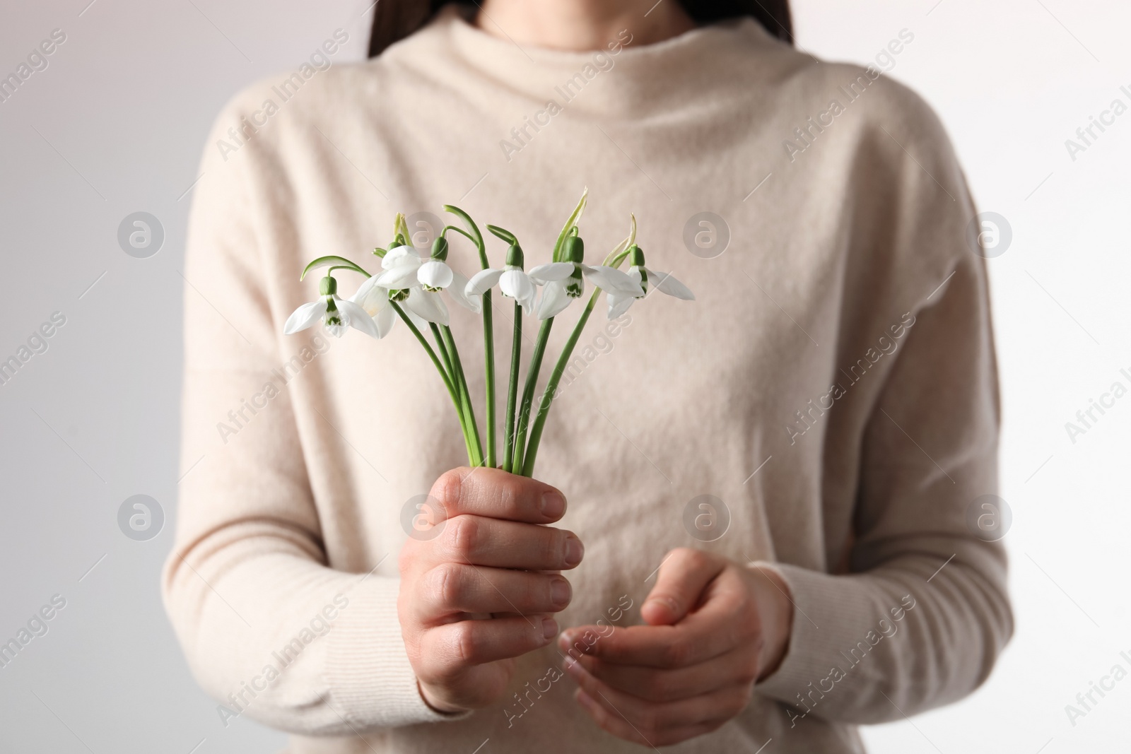 Photo of Woman holding beautiful bouquet of snowdrops on light background, closeup