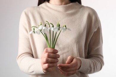 Woman holding beautiful bouquet of snowdrops on light background, closeup