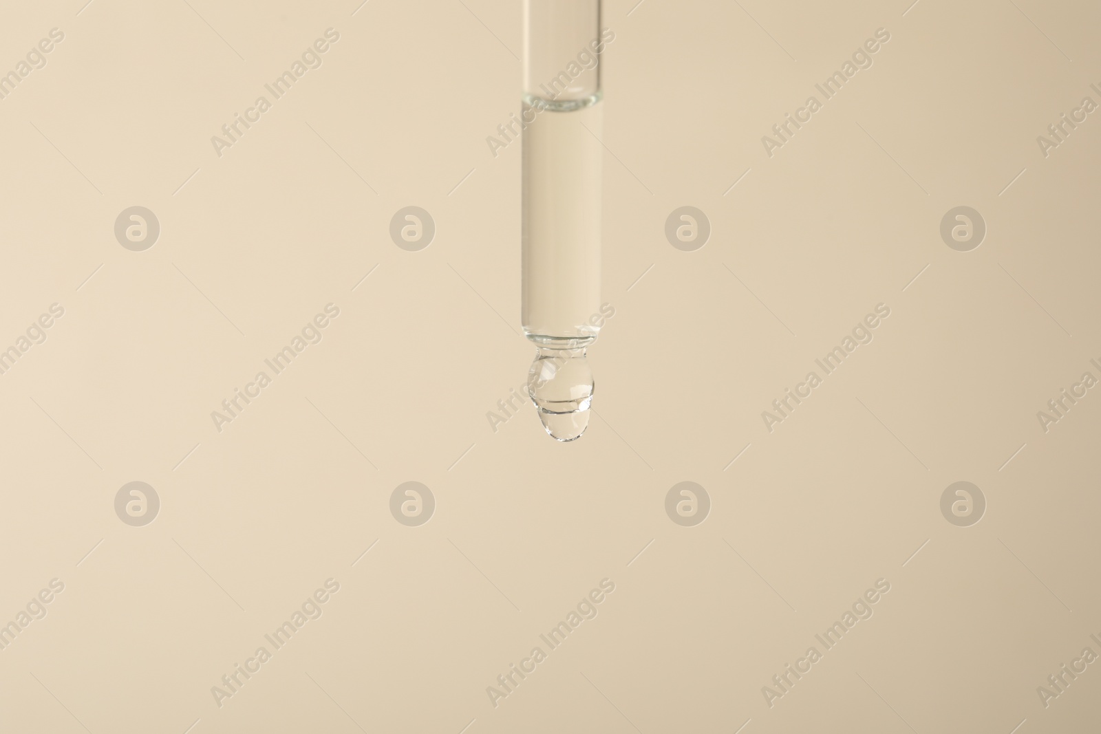 Photo of Dripping cosmetic serum from pipette on beige background, space for text