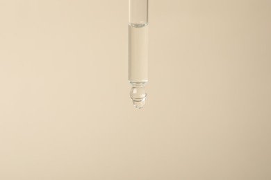 Photo of Dripping cosmetic serum from pipette on beige background, space for text