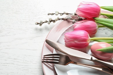 Festive Easter table setting with flowers on wooden background, above view. Space for text