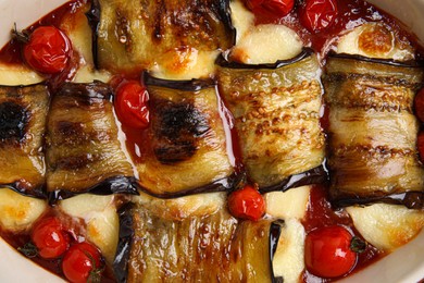 Photo of Tasty eggplant rolls with tomatoes and cheese in baking dish, top view