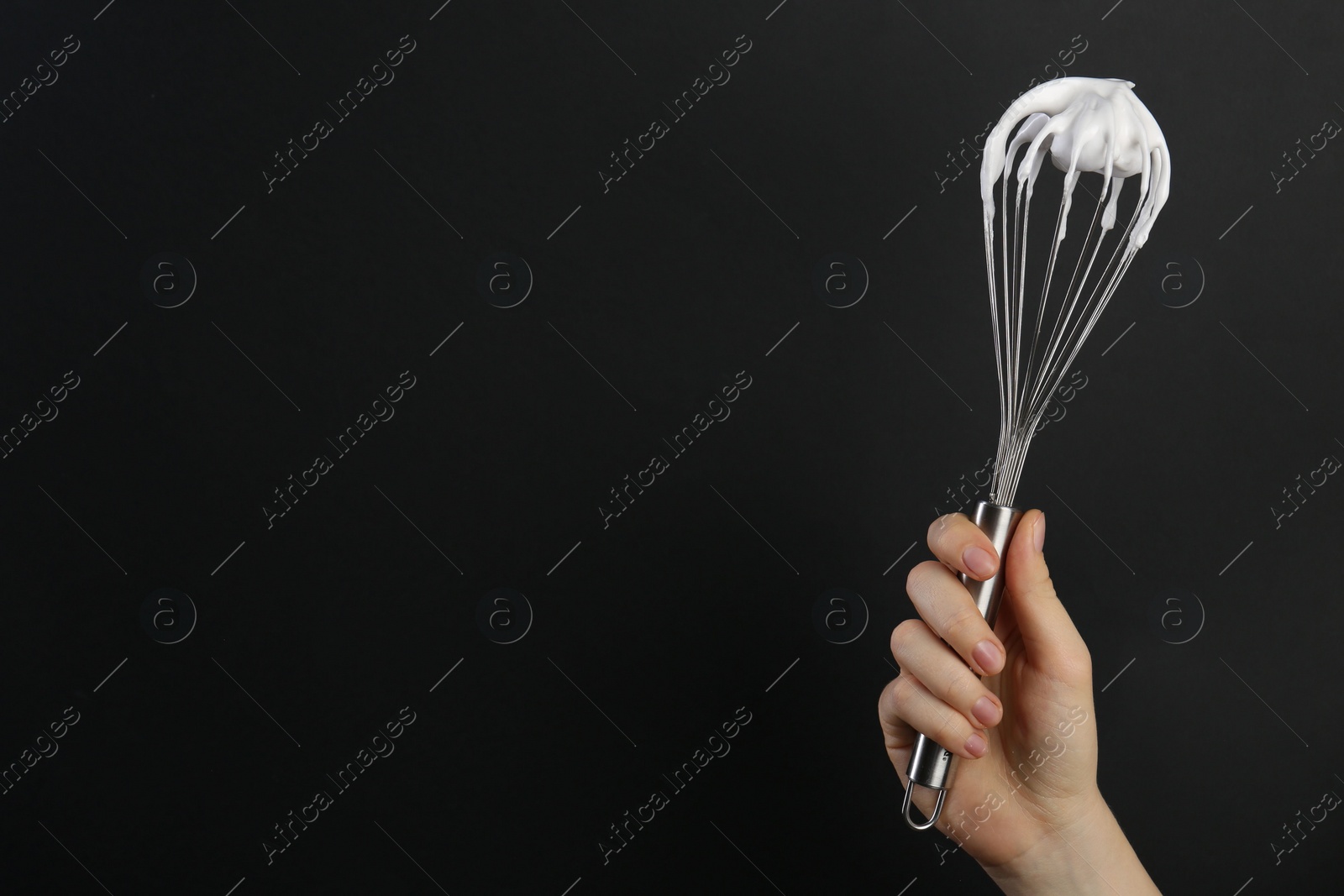 Photo of Woman holding whisk with whipped cream on black background, closeup. Space for text