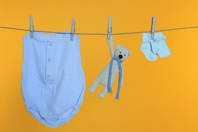 Photo of Baby clothes and toy drying on laundry line against orange background