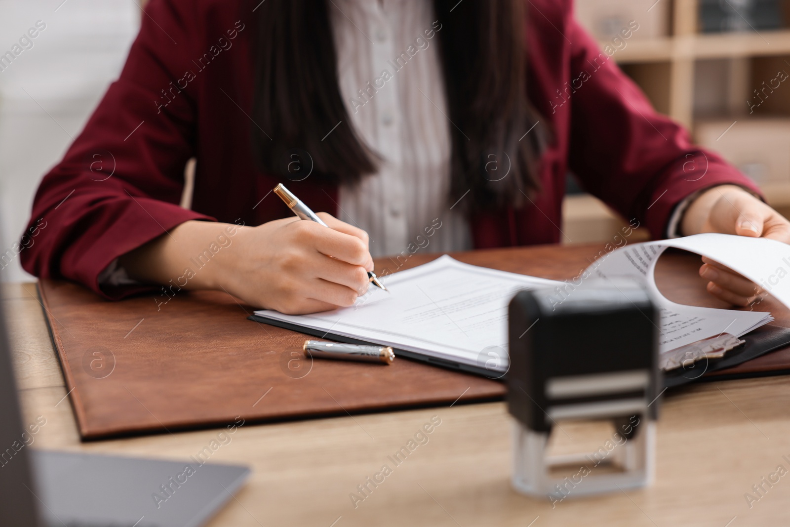 Photo of Notary signing document at table in office, closeup