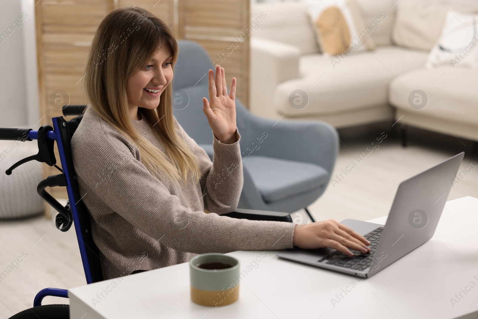 Photo of Woman in wheelchair having video chat via laptop at table in home office