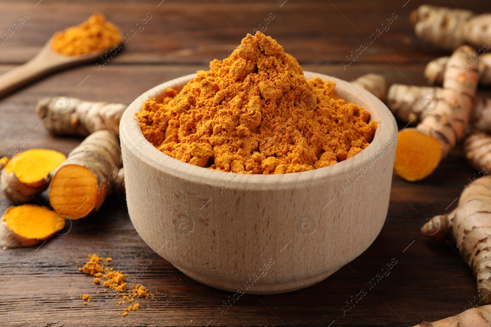 Photo of Bowl with turmeric powder and raw roots on wooden table, closeup