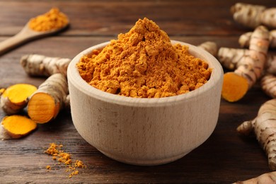 Bowl with turmeric powder and raw roots on wooden table, closeup