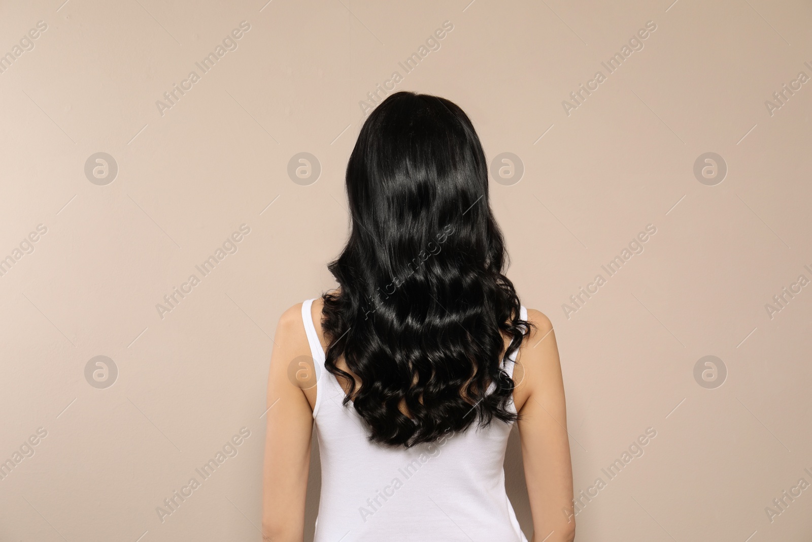 Photo of Young woman with long curly hair on beige background, back view