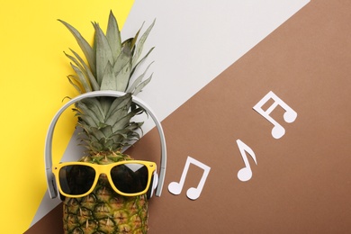 Photo of Funny pineapple with headphones and sunglasses on color background, flat lay