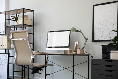 Photo of Comfortable office chair near desk with modern computer indoors