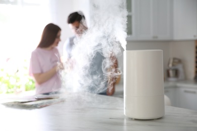Modern air humidifier and blurred couple in kitchen