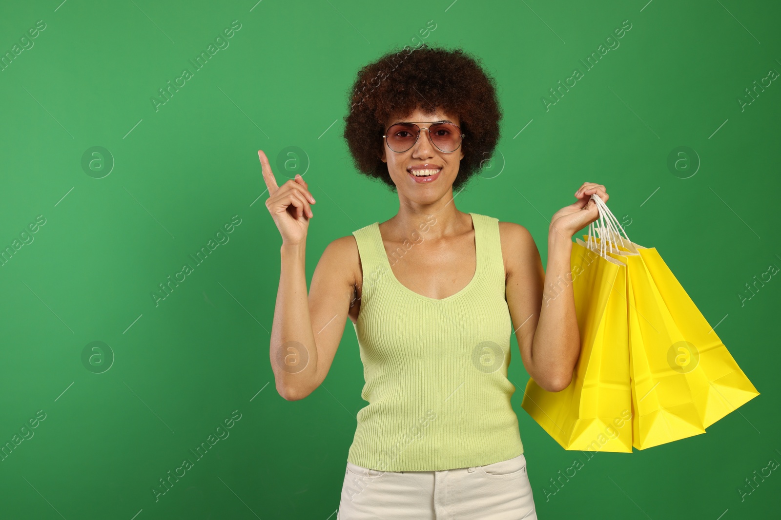 Photo of Happy young woman with shopping bags pointing at something on green background. Space for text