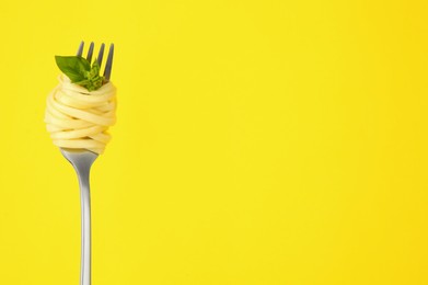 Photo of Fork with tasty pasta and basil on yellow background, space for text