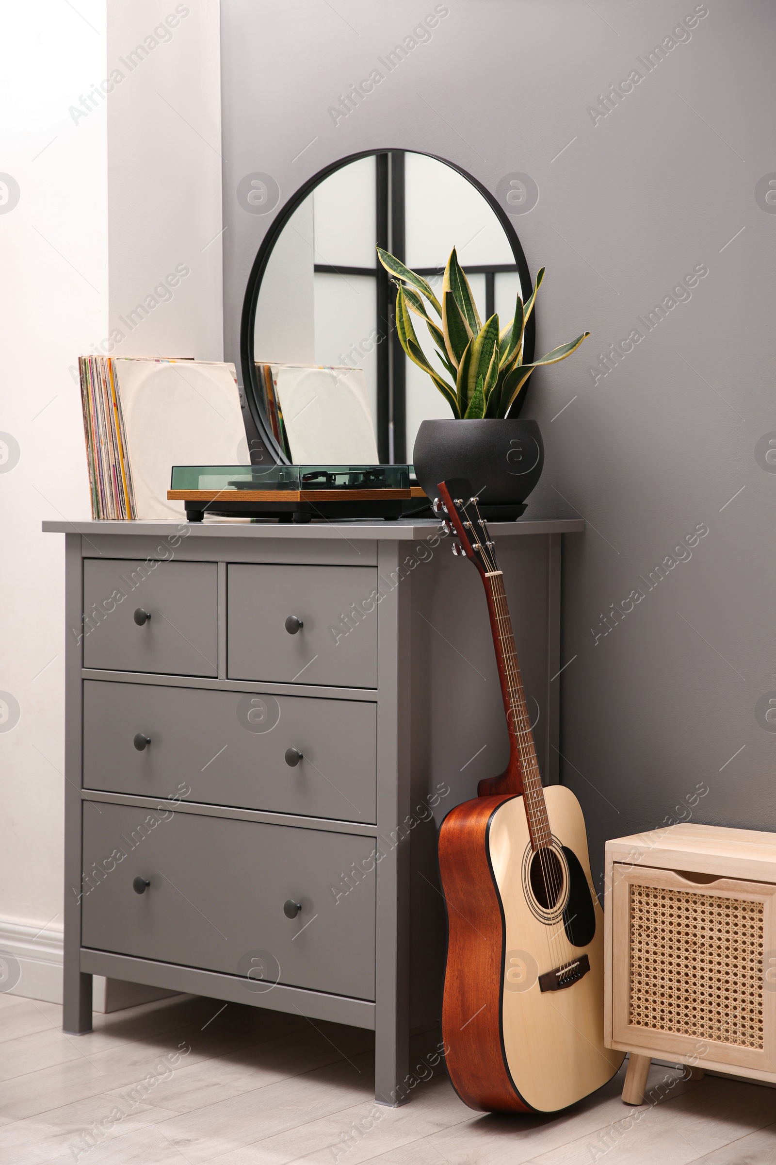 Photo of Stylish turntable, guitar and vinyl records on chest of drawers indoors