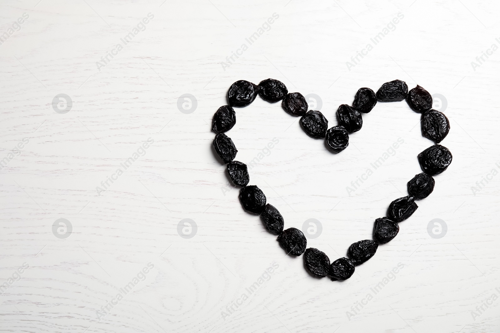 Photo of Heart shaped frame of sweet dried plums on wooden background, top view with space for text. Healthy fruit