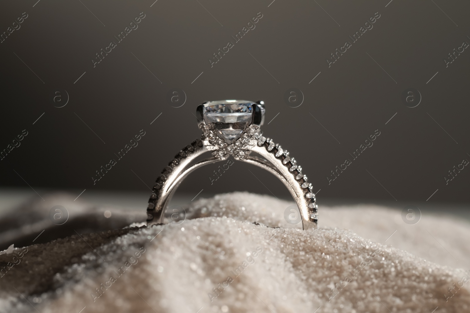 Photo of Luxury jewelry. Stylish presentation of ring in sand against grey background, closeup