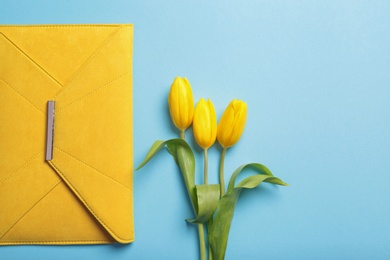 Photo of Flat lay composition with stylish woman's clutch and spring flowers on color background, space for text