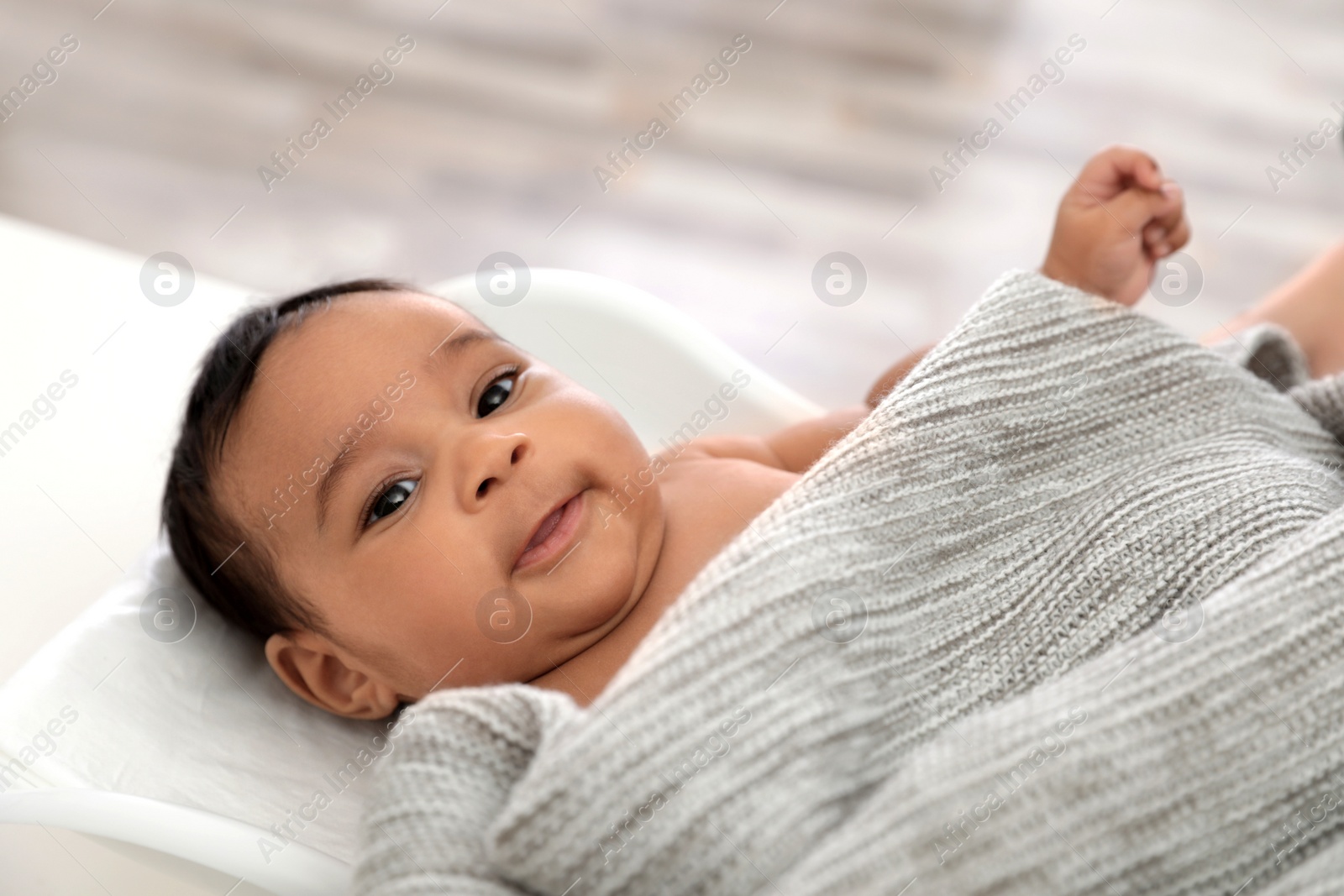 Photo of Cute African-American baby lying on scales indoors