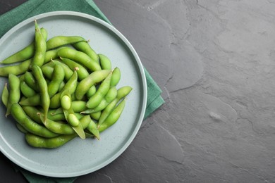 Photo of Plate of green edamame beans in pods on black table, top view. Space for text