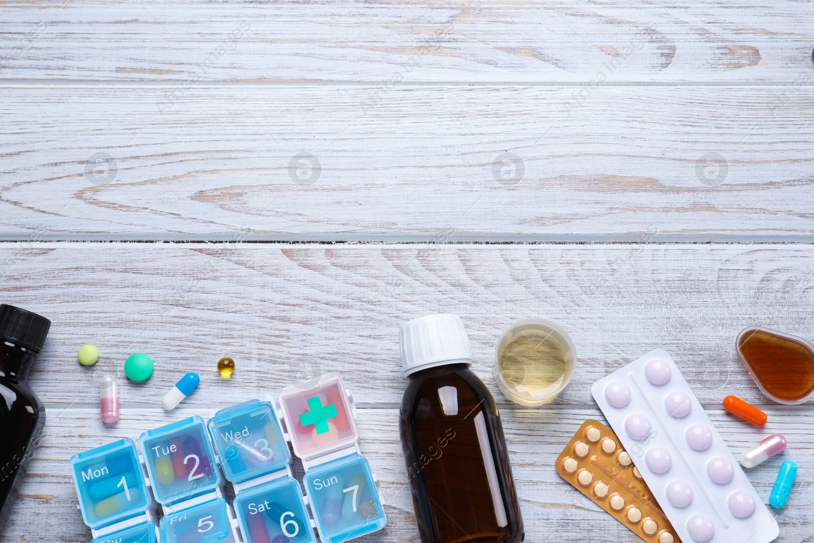 Photo of Flat lay composition with bottles of syrup, measuring cup and pills on white wooden table, space for text. Cold medicine