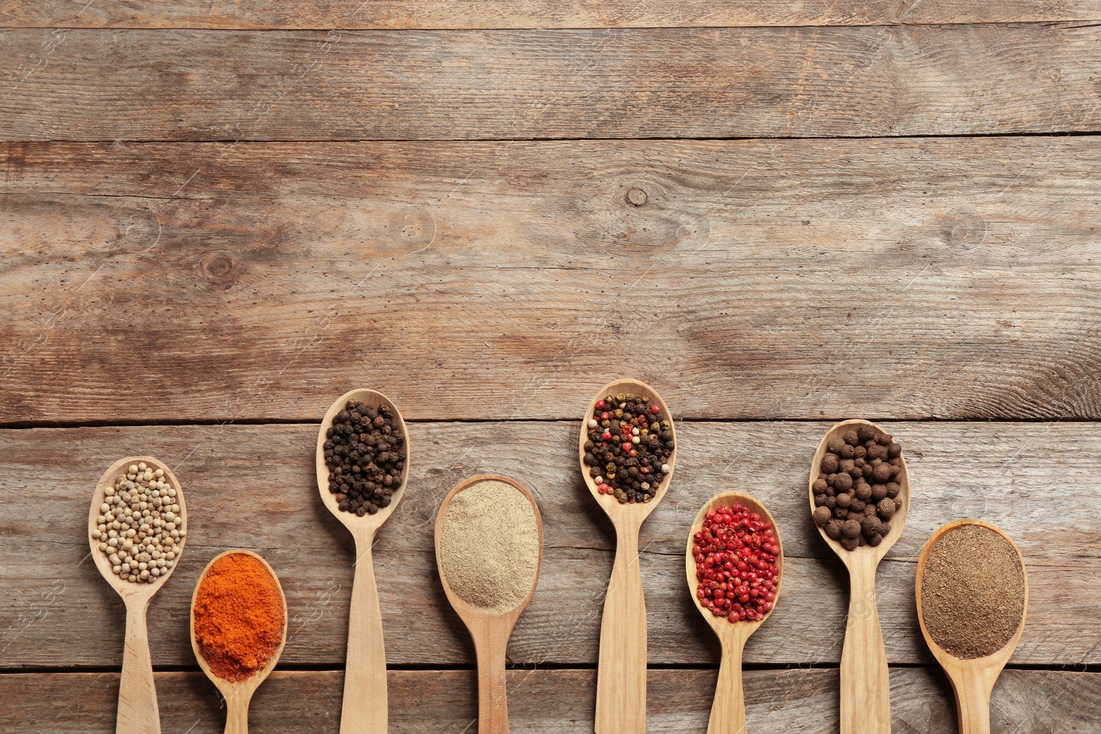 Photo of Spoons with different types of pepper and space for text on wooden background, top view