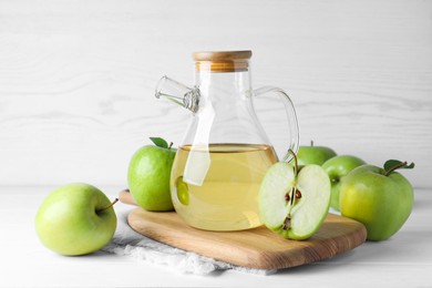Photo of Jug of tasty juice and fresh ripe green apples on white wooden table