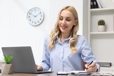 Happy secretary taking notes while working with laptop at table in office