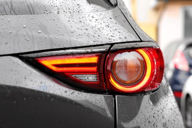 Photo of Car with switched on tail light in drops of water outdoors, closeup