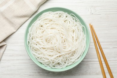 Photo of Bowl with cooked rice noodles and chopsticks on white wooden table, flat lay