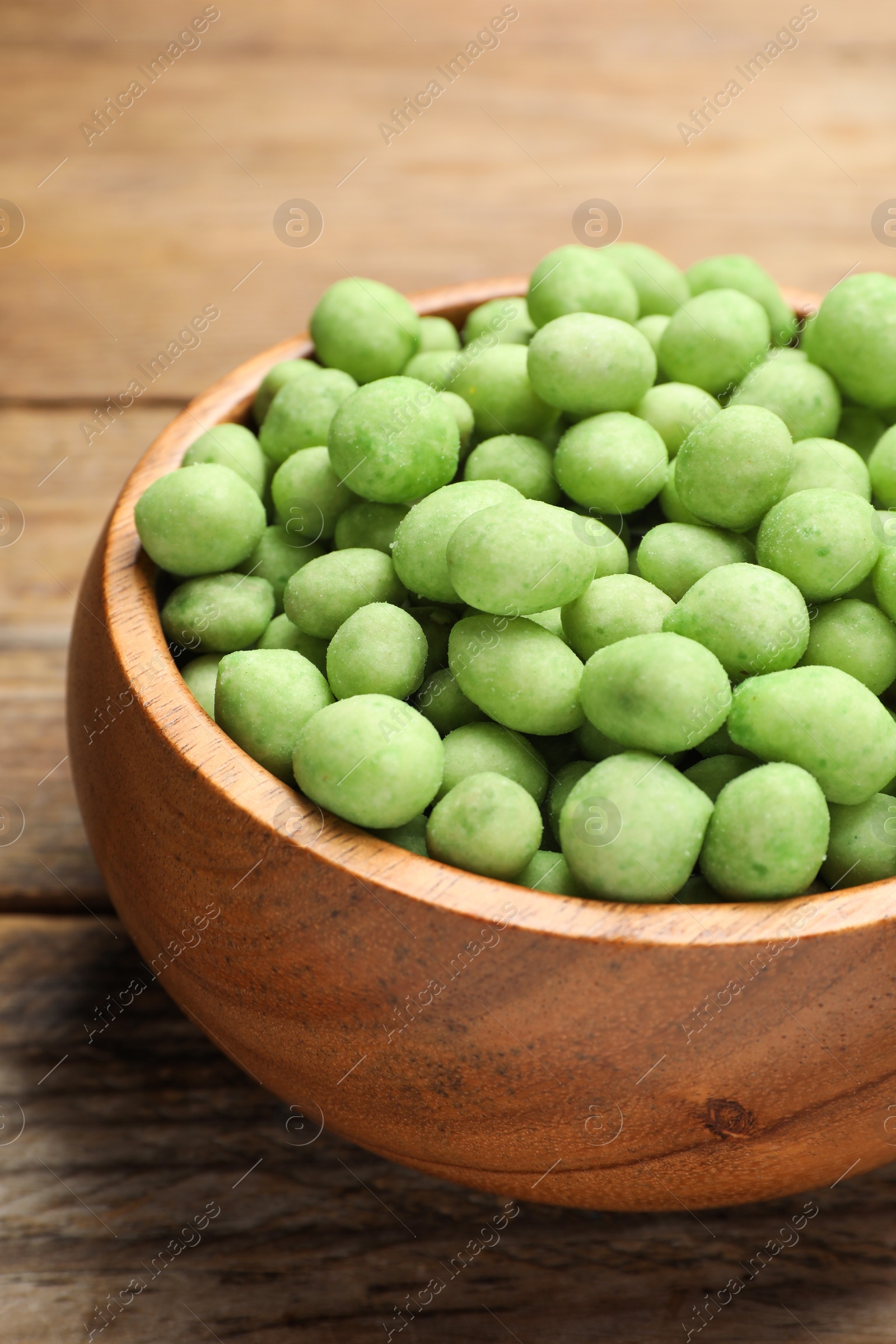 Photo of Tasty wasabi coated peanuts on brown wooden table, closeup
