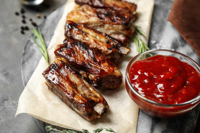 Delicious grilled ribs with sauce served on grey table, closeup