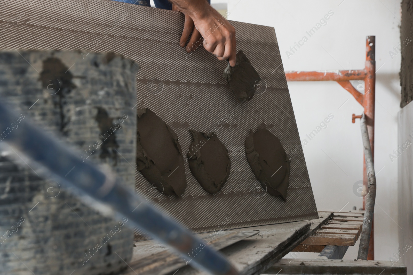 Photo of Worker applying cement on wall tile for installation indoors, closeup