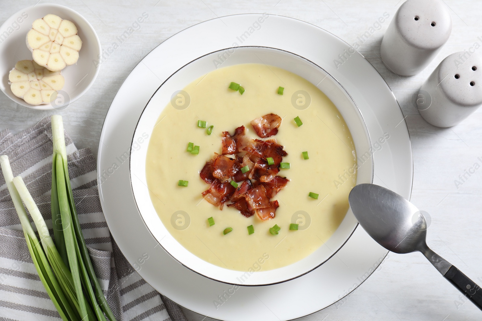 Photo of Tasty potato soup with bacon in bowl served on white wooden table, flat lay