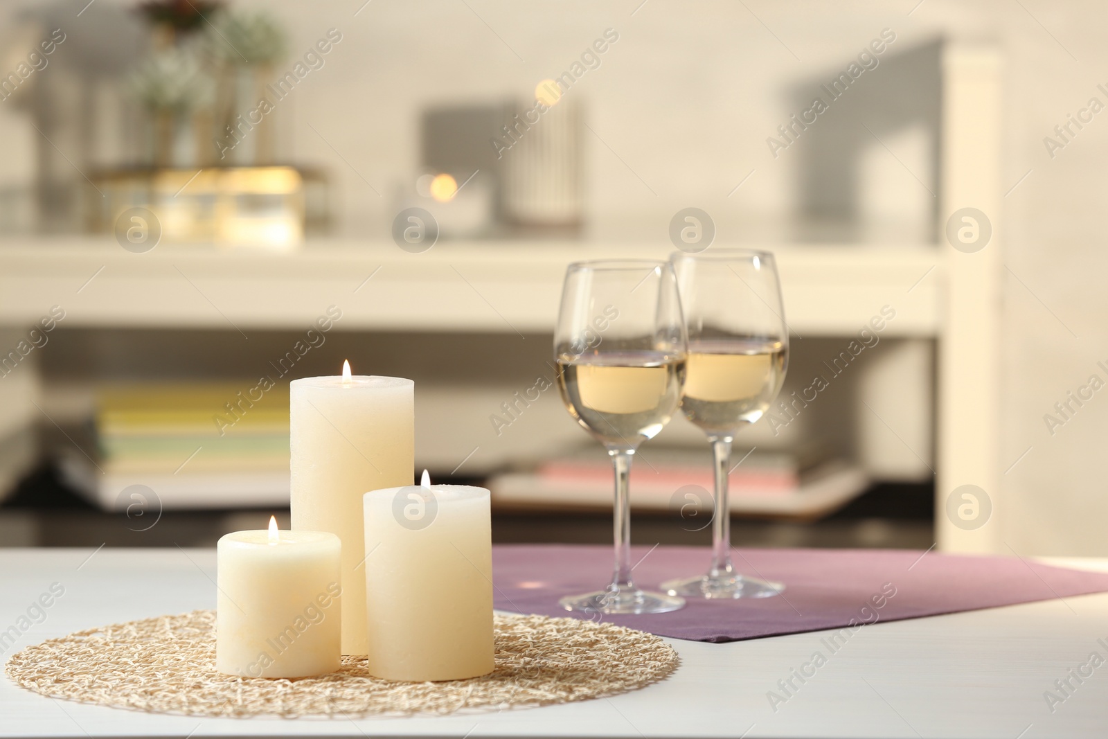 Photo of Burning candles and glasses of wine on white table indoors