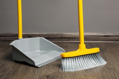 Photo of Sweeping wooden floor with plastic broom and dustpan indoors
