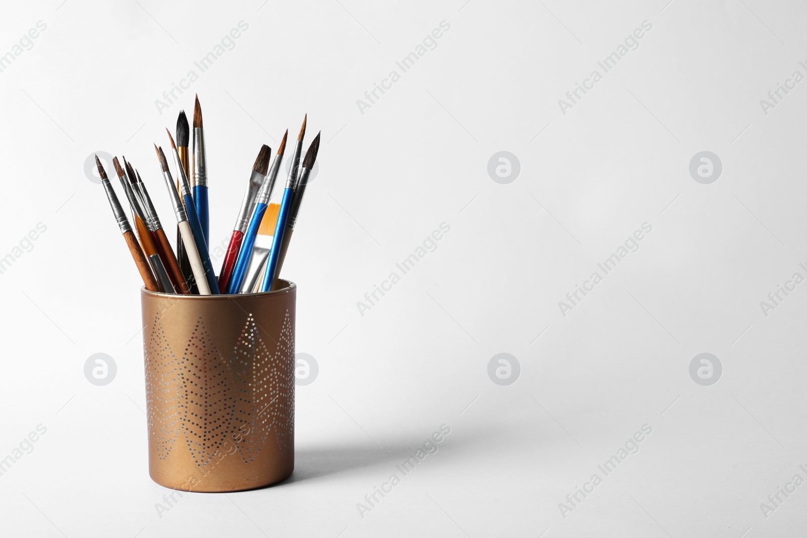 Photo of Holder with different paint brushes on white background. Space for text