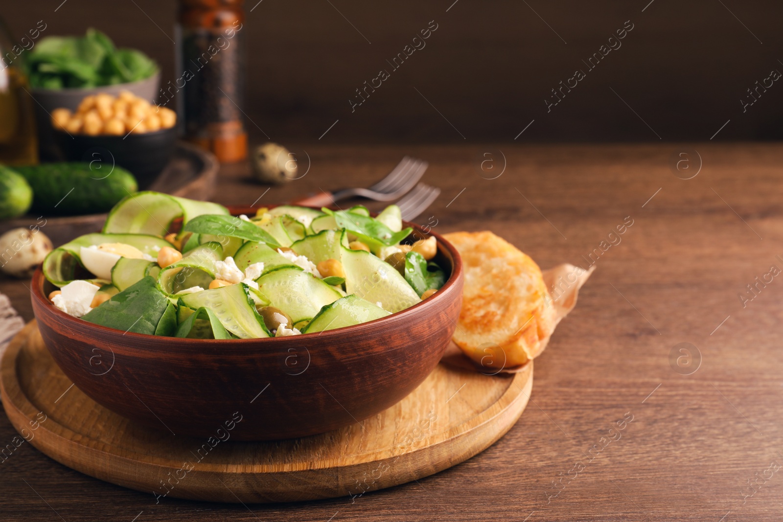 Photo of Delicious cucumber salad and rosted bread served on wooden table. Space for text