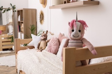 Toy unicorn on comfortable bed in child's room, space for text. Interior design