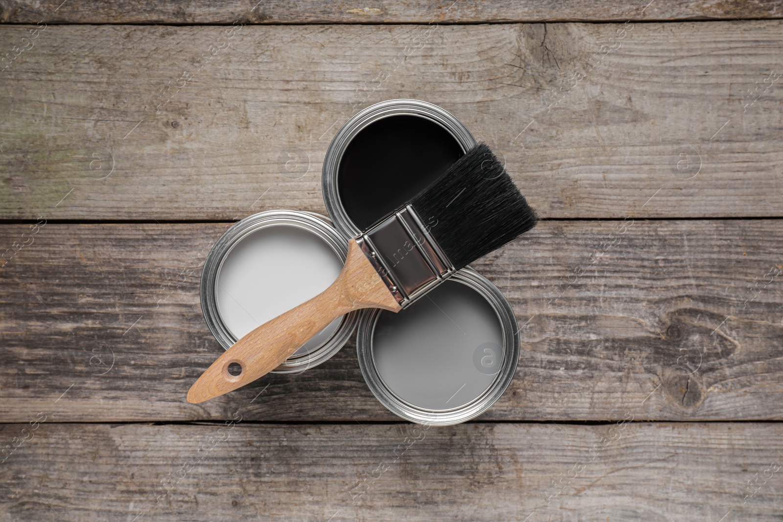 Photo of Cans of white, black and grey paints with brush on wooden table, flat lay