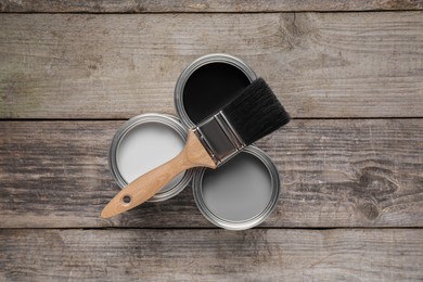Cans of white, black and grey paints with brush on wooden table, flat lay