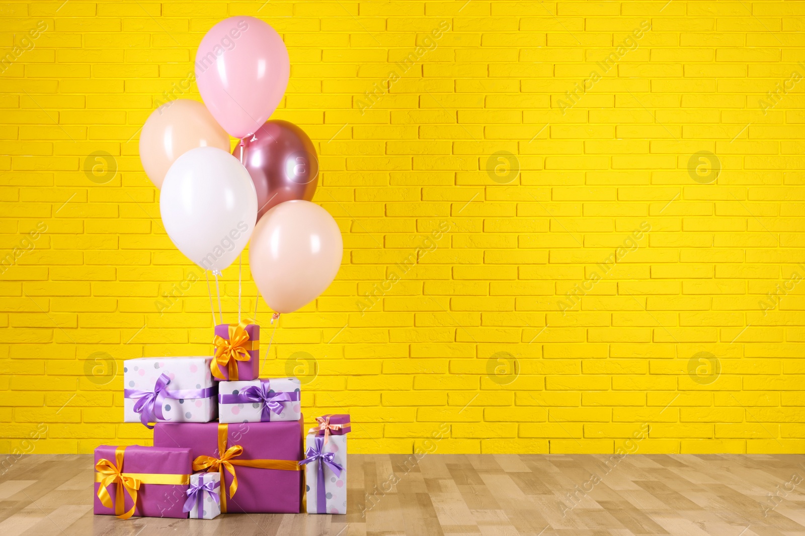 Photo of Many gift boxes and balloons near yellow brick wall. Space for text