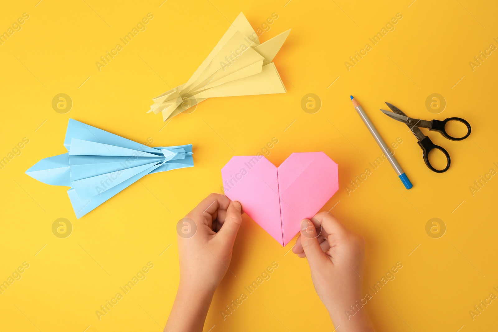 Photo of Origami art. Child holding paper figure on yellow background, closeup and top view