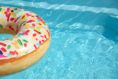 Photo of Bright inflatable doughnut ring floating in swimming pool on sunny day. Space for text