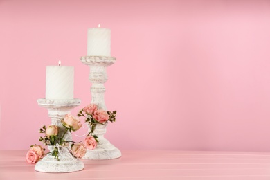 Photo of White candlesticks with burning candles and floral decor on pink wooden table. Space for text