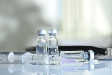 Photo of Glass vials, syringe and stethoscope on white table, closeup