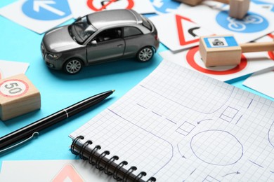 Photo of Different road signs, notebook with sketch of roundabout and toy car on light blue background. Driving school