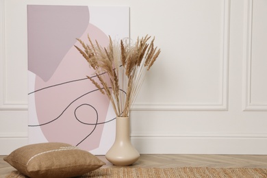 Photo of Fluffy reed plumes and painting near white wall indoors, space for text. Interior elements
