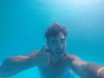 Handsome young man swimming in pool, underwater view