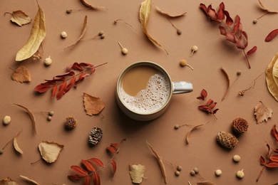 Flat lay composition with cup of hot drink and autumn leaves on brown background. Cozy atmosphere